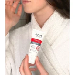 Femme en peignoir appliquant la crème réparatrice ACM Sébionex Hydra sur son visage.