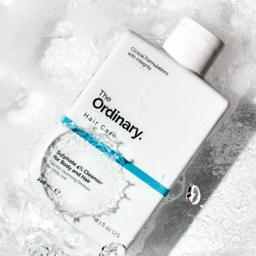 Flacon de nettoyant Sulfate 4% The Ordinary immergé dans de l'eau, illustrant son usage pour le corps et les cheveux.