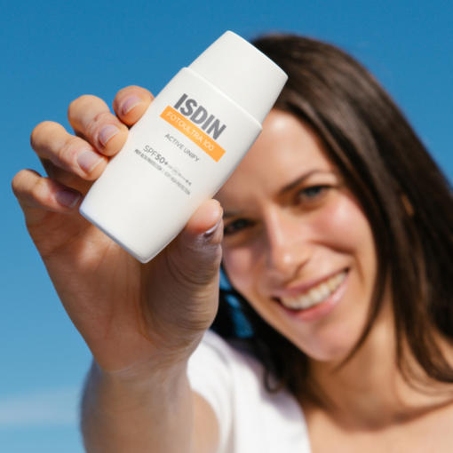Femme souriante montrant la crème ISDIN Fotoultra 100 Active Unify SPF 50+.