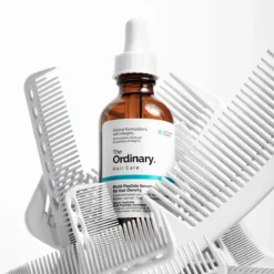 Flacon de The Ordinary Multi-Peptide Serum for Hair Density posé sur des peignes blancs empilés.